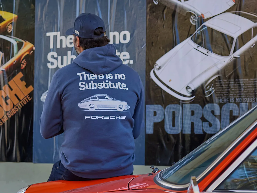 Cliente com moletom Porsche “There is no Substitute.” sentado sobre um Porsche 911 clássico laranja